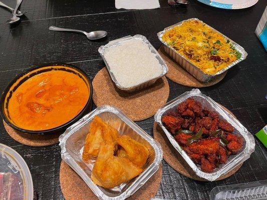 Clockwise from orange dish Butter chicken, complimentary rice, Chicken Biryani Rice, Chicken 65, Vegetable Samosa.