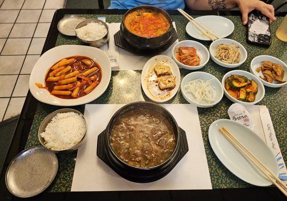 Korean meal including side dishes, tteokbokki, bulgogi ttukbaegi, and kimchi jjigae