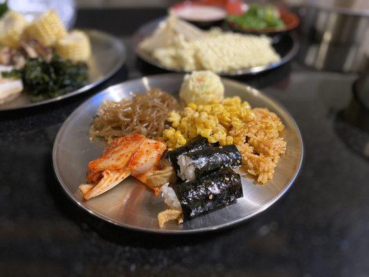 Hot dishes including kimichi, kimichi fried rice, corn, potato salad, and japachae.