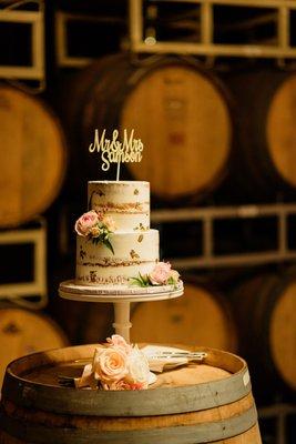 A gorgeous wedding cake made even more memorable with a backdrop of barrels. Photo by Dan Phan Photography.