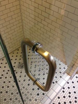 Brushed nickel handle with polished aluminum accents used on a frameless shower enclosure.