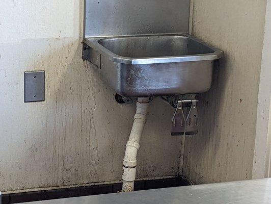 Hand washing sink near the front counter. Note the dirt on the walls.