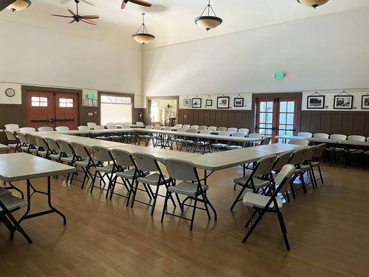 Auditorium with tables set up in a square with the center open. Chairs line the tables and the room.