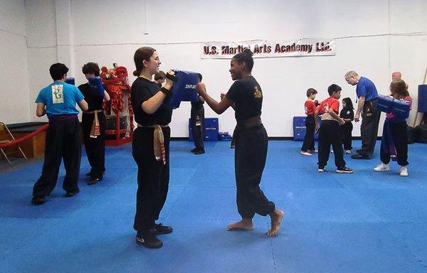 Family Kung Fu class for children about 7 years old through adult practicing self-defense moves with a partner.