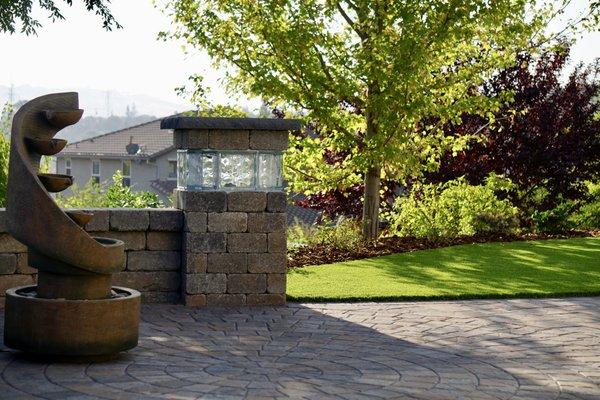 Elegant column sitting wall with built-in lighting element, plus paved circle kit hardscaped backyard patio.