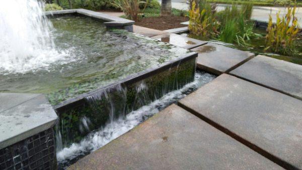 Infinity waterfall flowing down between stepping stones into small carp pond.