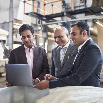 3 executive coaching clients around laptop in factory