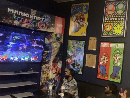 People playing Mario Kart and the nostalgic Super Mario 3 poster on the wall