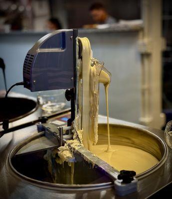 Big mixer bowl of chocolate as seen through glass. Customers can mix a variety of combinations to make a custom chocolate bar.