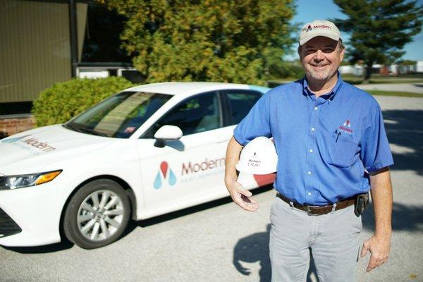 Technician smiling ,holding helmet with Modern Pest Branded car in the background