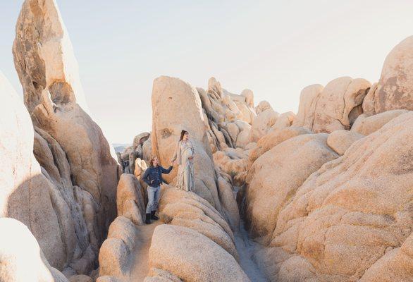 Here is a landscape shot of a couple in Joshua tree national park climbing its iconic boulders. this is a maternity photo shoot.