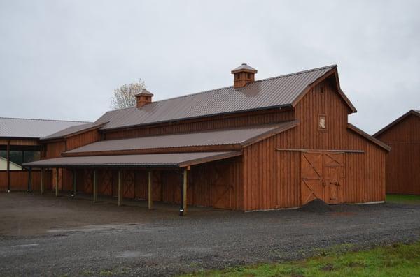 Custom horse barn with board and bat wood siding and roof cupolas for an added touch. Shed row cover for horse runs.