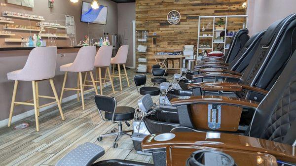 Interior of the salon with manicure stations (plexiglass shields all along the bar) and pedicure stations.