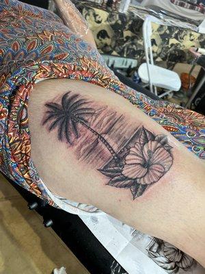 Palm tree and beach scene tattoo on the thigh.