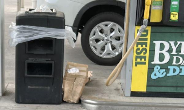 Overflowing trashcan and debris on the ground at the gas pump