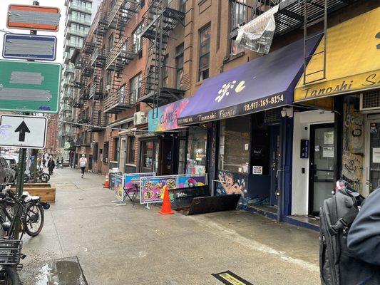 It's actually the minimal storefront to the left of the blue awning. Few doors from Tanoshi Sushi.