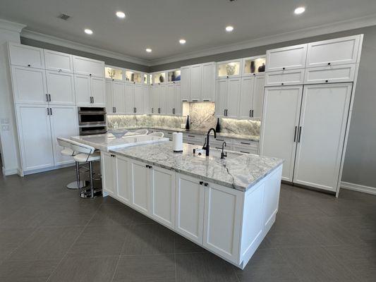 White shaker cabinets, paneled refrigerator, stacked uppers with glass and lighting.