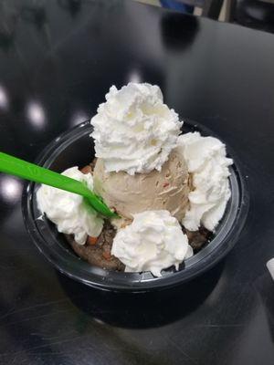 Coffee ice cream with fruity pebble and peanut butter cup mix-ins on top of an M&M oreo cookie, with whipped cream on top.