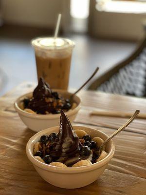 Small açaí bowl with blueberry, banana, granola, and condensed milk. Delicious iced Lavender Honey latte in the back.