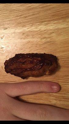 A boys pinky next to the worlds smallest over cooked lightly drizzled bbq chicken wing