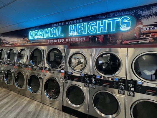 Dryers along a wall with a Normal Heights mural and neon sign