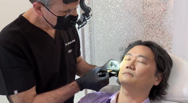 Dr. Castelli injecting Dr. Lee with Voluma to add volume to Dr. Lee's cheeks.