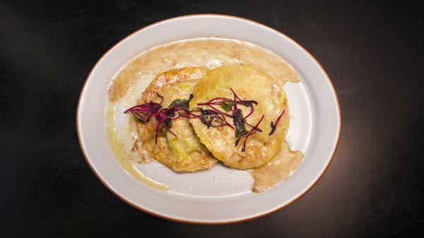 Two large, handmade ravioli stuffed with ricotta, spinach, an over-easy egg, in a brown butter truffle sauce