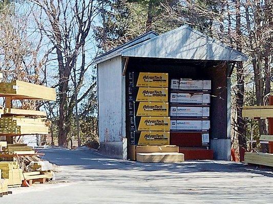 A shed housing neatly stacked AdvanTech subflooring and sheathing products, surrounded by racks of construction materials in ...