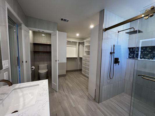 Master BA with curbless shower, fully tiled floor and walls, walk-in closet organizer; toilet fully tiled with floating shelves.