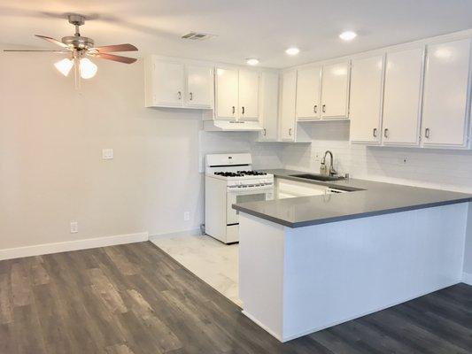 A stunning remodeled kitchen with brand new grey hardwood floors, quartz countertops, tile flooring in kitchen and freshly painted cabinets.