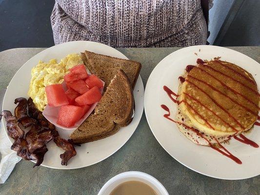 Scrambled eggs, bacon and toast with fruit and a raspberry swirl specialty pancake