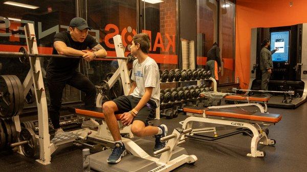 Trainer John offers guidance and tips as his client prepares for a proper and safe bench press session.