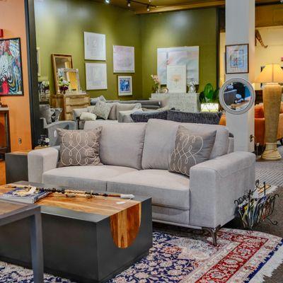 Modern living room furniture display area featuring an elegant grey sofa, surrounded by various decor items like rustic coffee tables.