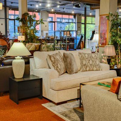 Furniture store with various sofas, chairs and lamps displayed in the background. The foreground features a comfortable & elegant sofa.