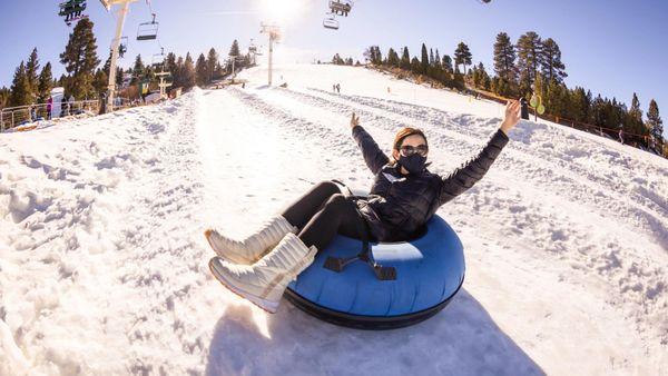 Hands raised high as you glide down on a winter snow tube.