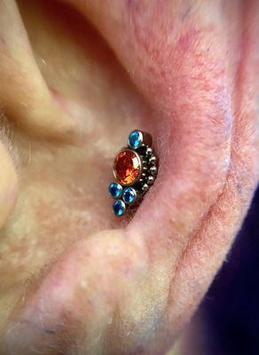 Conch piercing with Titanium Saturn top with Aquamarine and Fire Orange Cubic Zirconia gems.