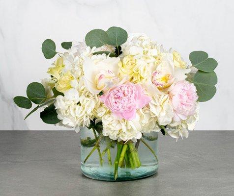 Cheyenne - White hydrangeas, pink peonies, cream white roses and pink peonies are accented by cymbidium orchids and silver dollars.