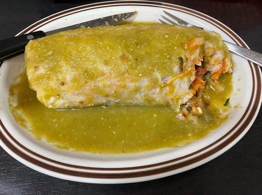 Wet al pastor burrito with green sauce filled with meat and rice.