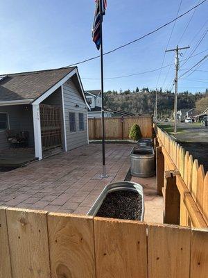 Small paved front yard with large solar powered flagpole and large horse watering containers moved from backyard.