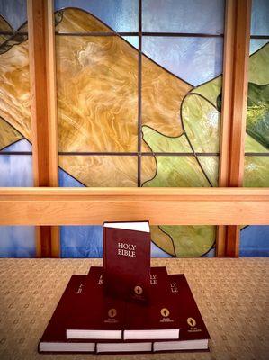 A mountain of free Gideon bibles in front of the stained glass mountains in the 2d floor chapel