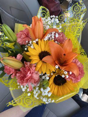 A wrapped bouquet of orange lilies and yellow sunflowers and more.