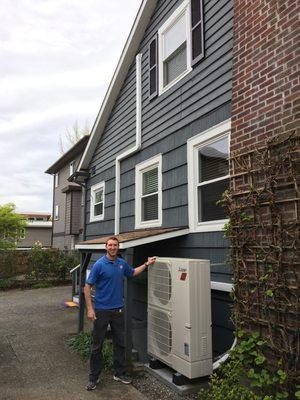 Branden standing in front of a Mitsubishi Hyper Heat system he help install.