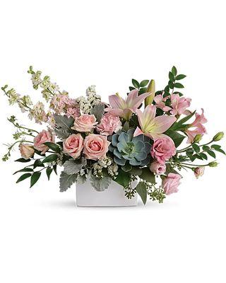 A wildly sophisticated array of pale pink roses and lilies with modern greens, it's perfectly presented in a simple white square vase.