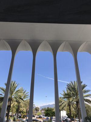 Arches attach to roof at the far end of the entrance with palm trees lining the parking area adjacent.