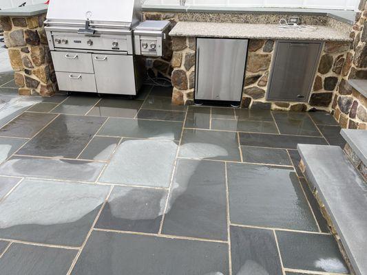 Slate patio installed so that water puddles in front of the grille area.