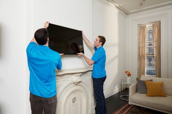 HD Installation technicians mounting television for customer in living room.