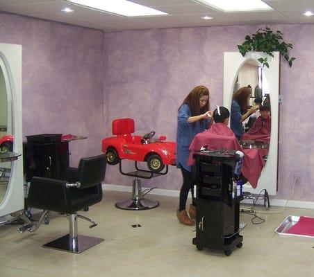 Young child getting a hair cut with red car ride in the background