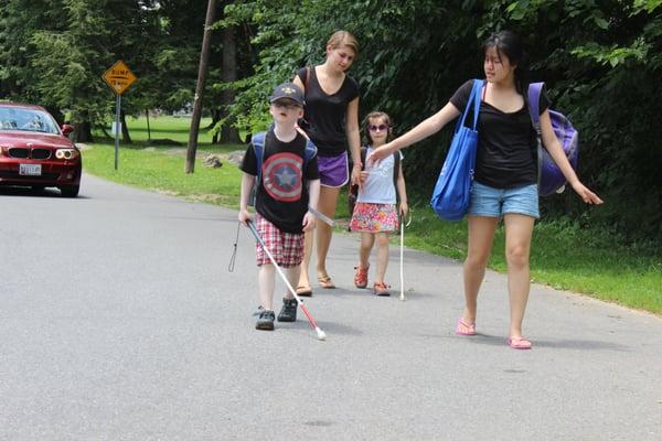 A young boy with a white cane walking with chaperones.