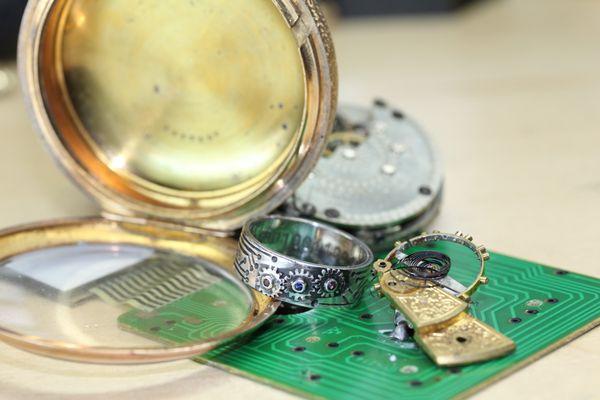 A custom silver ring, with interlocking gears, circuitry engraving around it, a special note in binary engraved inside and 3 birthstones