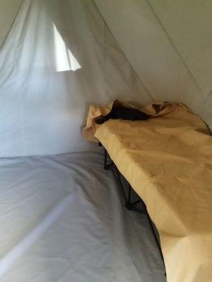 The inside of an 8x10 canvas Profile tent with a floor, showing a cot with a sleeping bag cover on it. The back window in back ground.